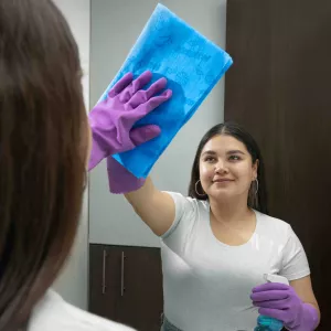 Mujer limpiando un viddrio de un espejo con tela magitel